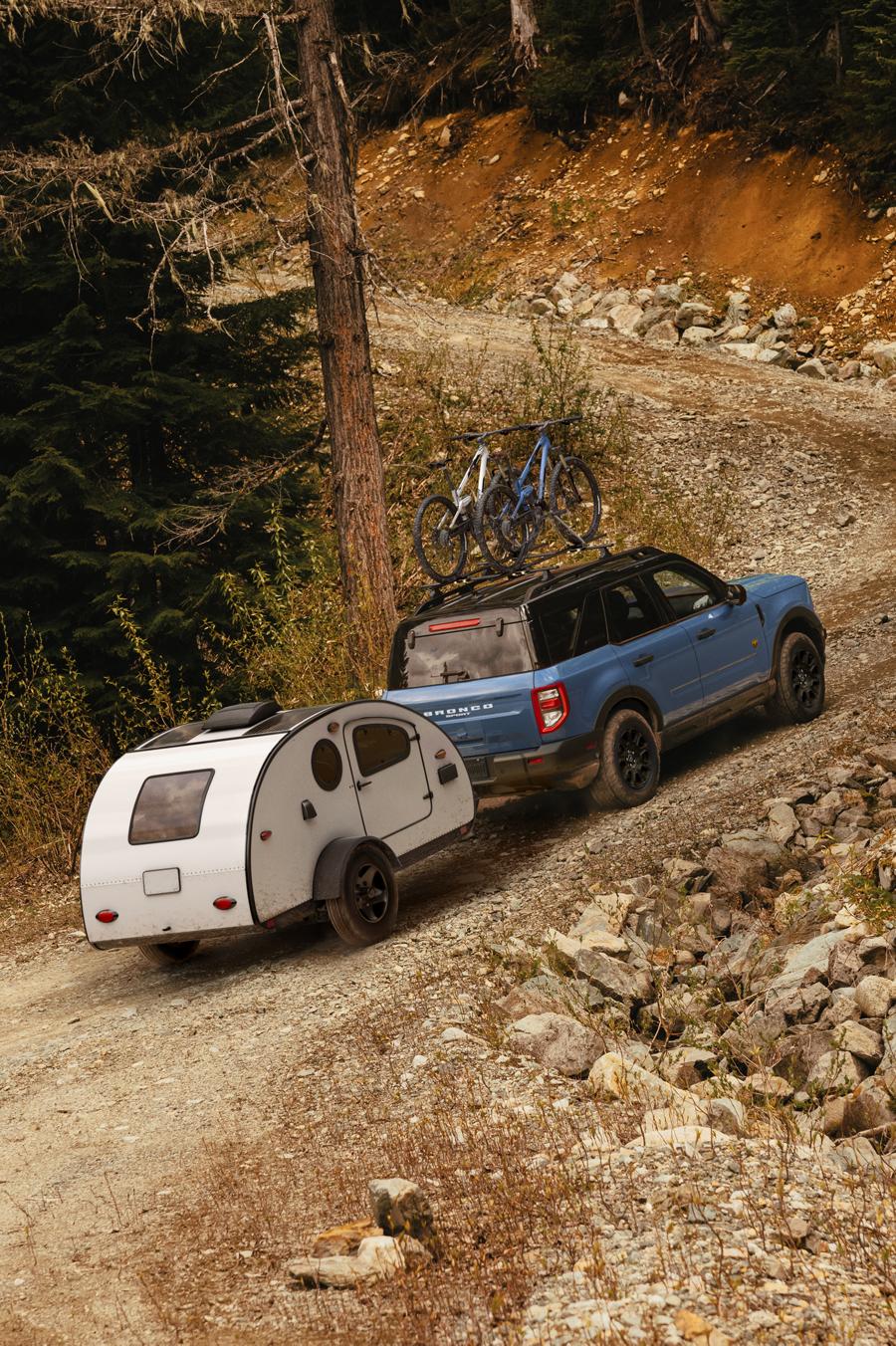 Ford Bronco Sport towing a small camper on a rocky trail with two mountain bikes on the roof